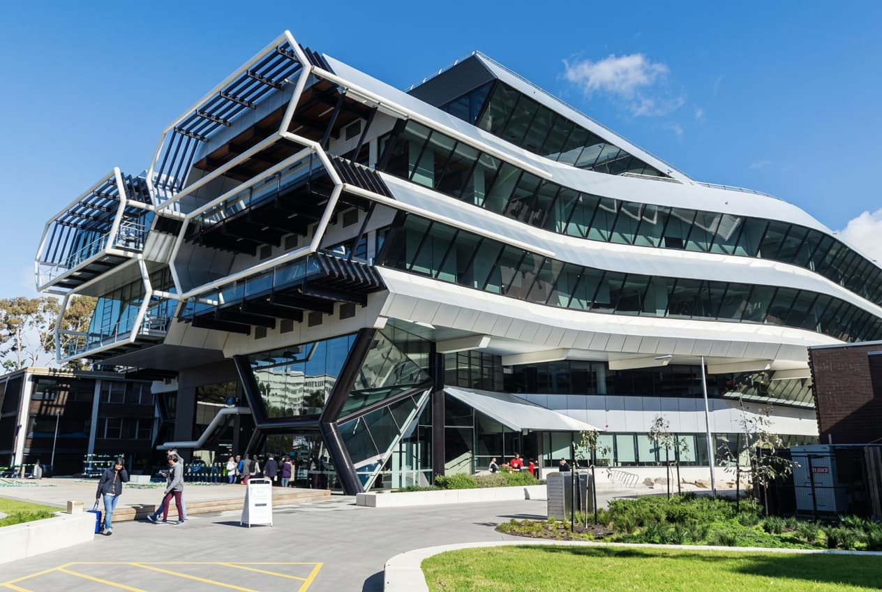 An angular glass and steel university building against a deep blue sky.