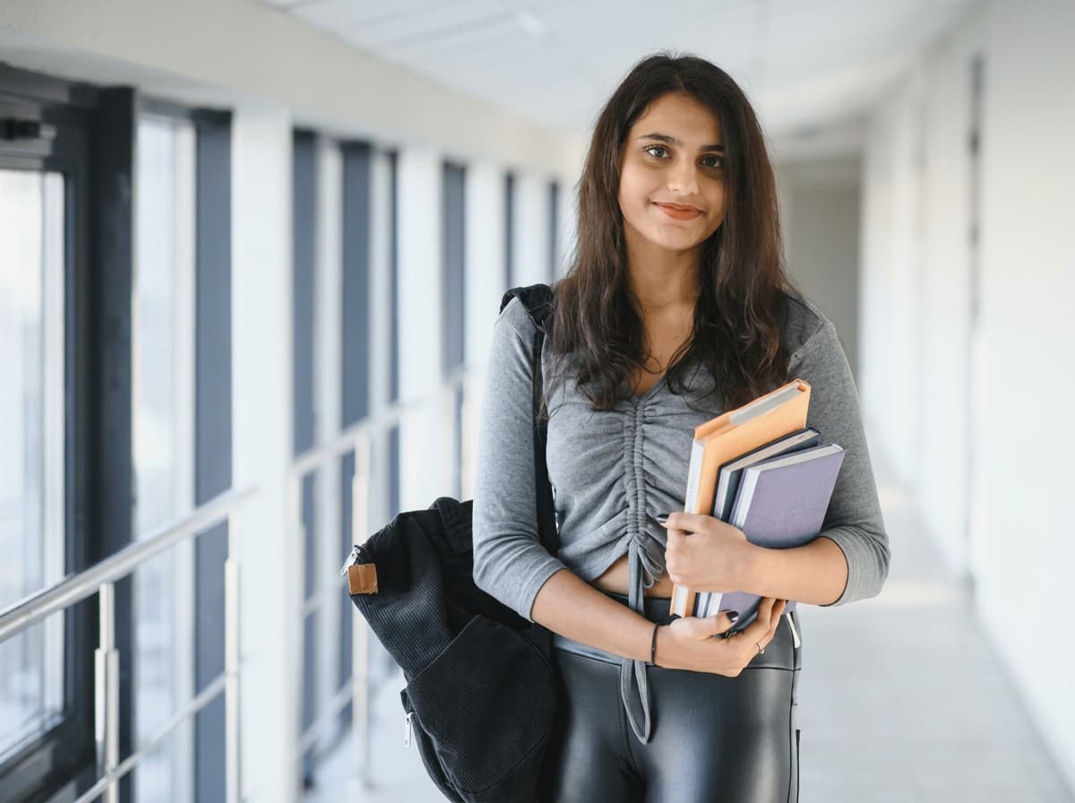 A student carrying books and a backpack in a bright university corridor.