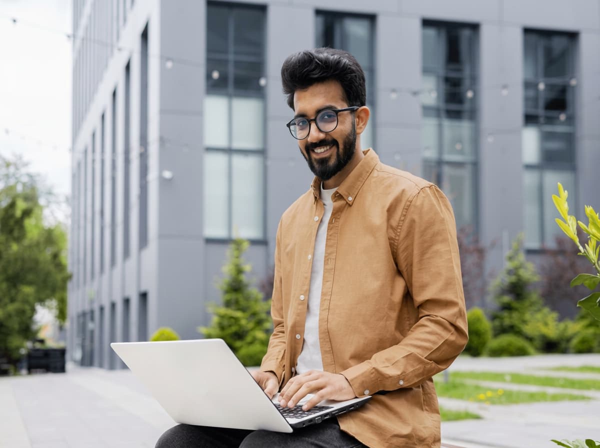 A student working through application documents on a laptop outside a modern building.