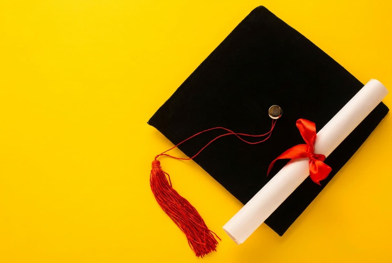 A graduation cap and diploma on a bright yellow background.