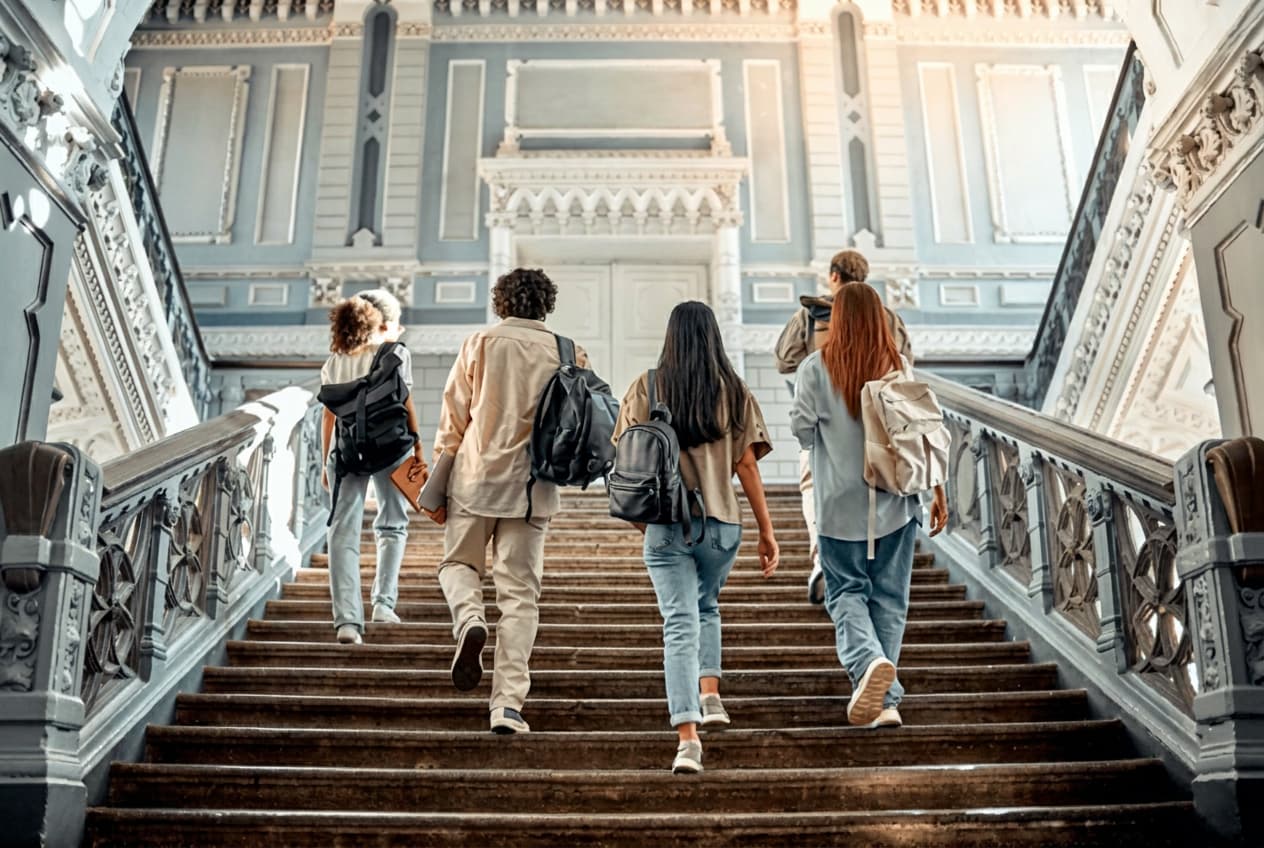 Five students climbing a grand balustraded staircase towards tall doors.