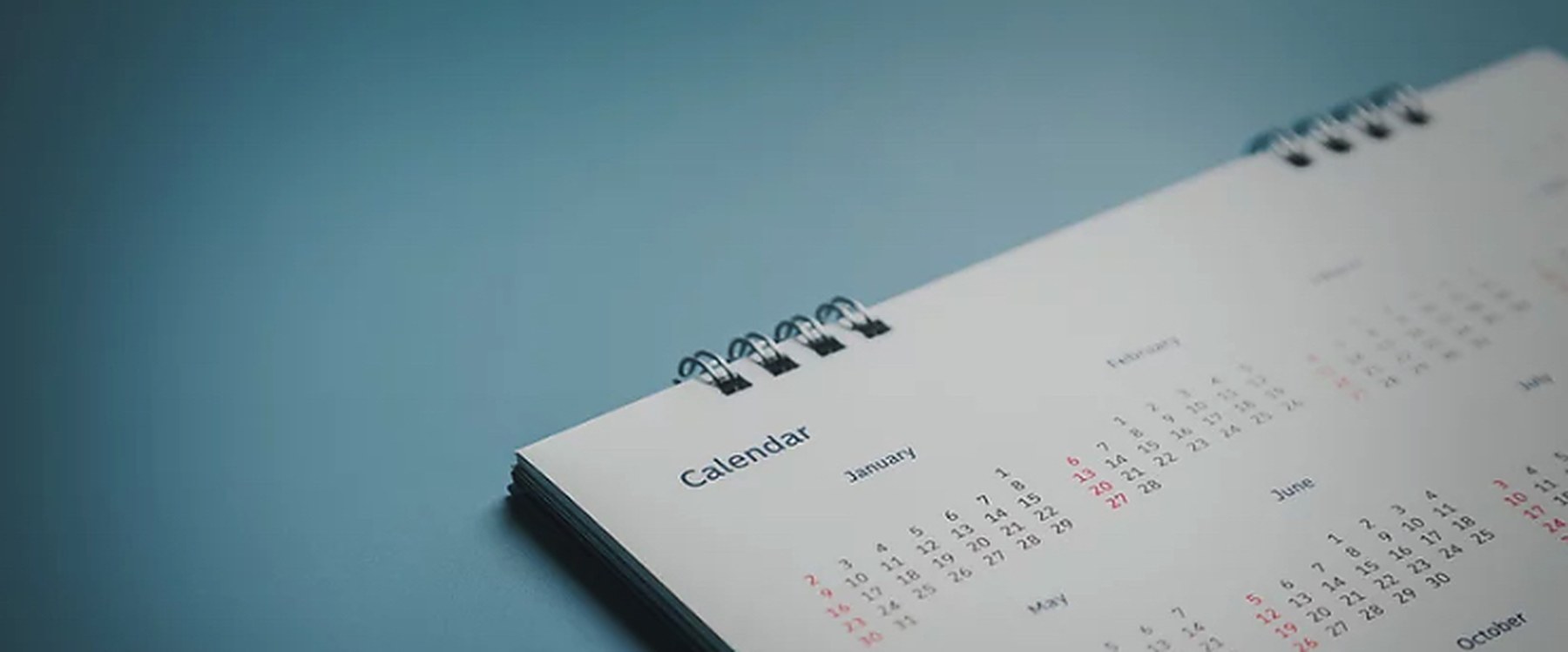 A spiral desk calendar open on a dusty blue desk.