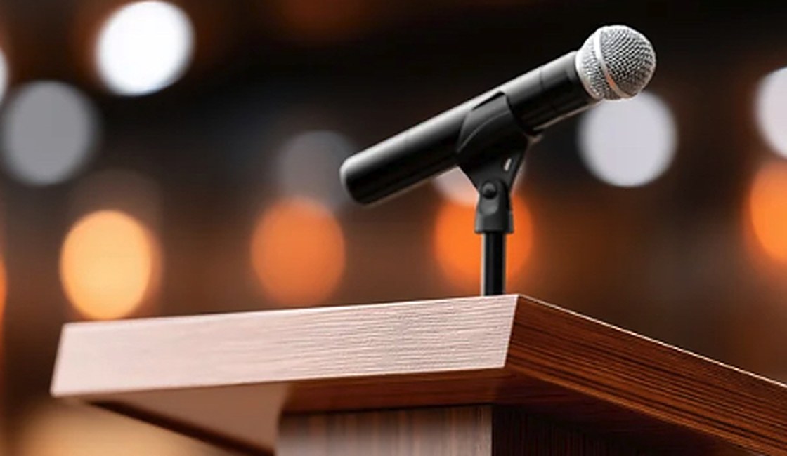 A microphone on a wooden lectern with warm stage lights behind it.