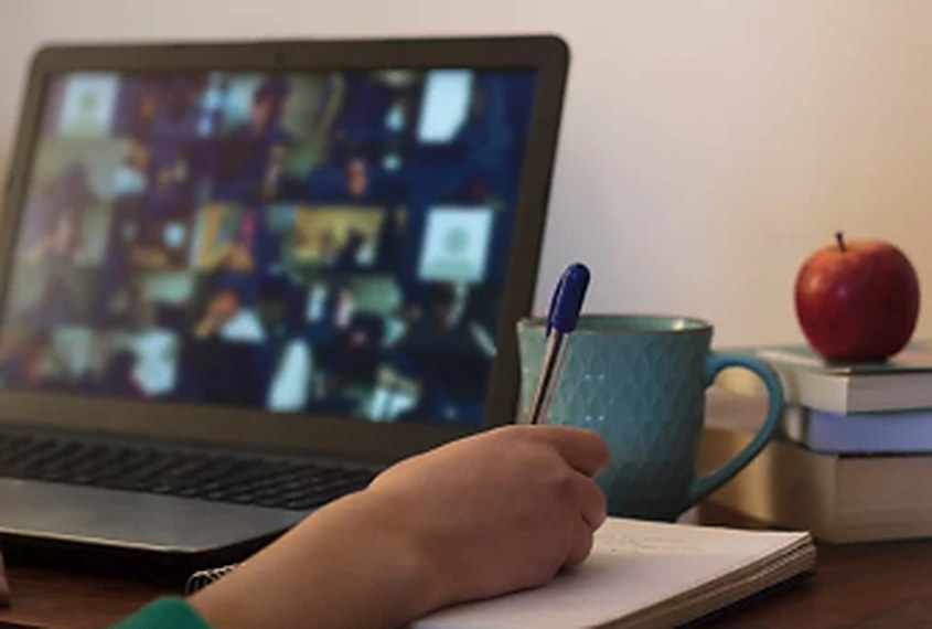 A hand writing notes in a notebook beside a laptop showing a video session.