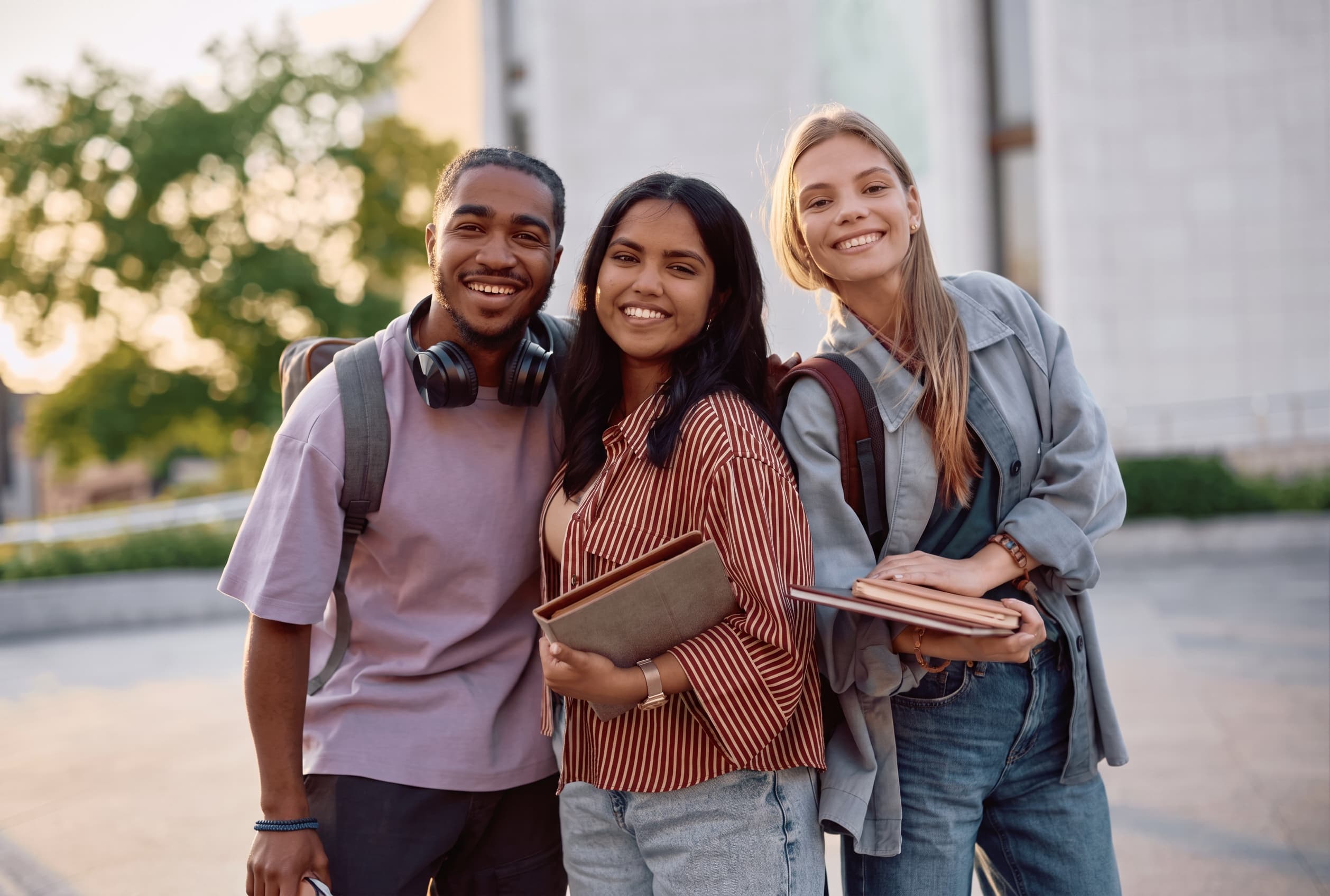 Three students standing together outside a campus building in warm afternoon light.