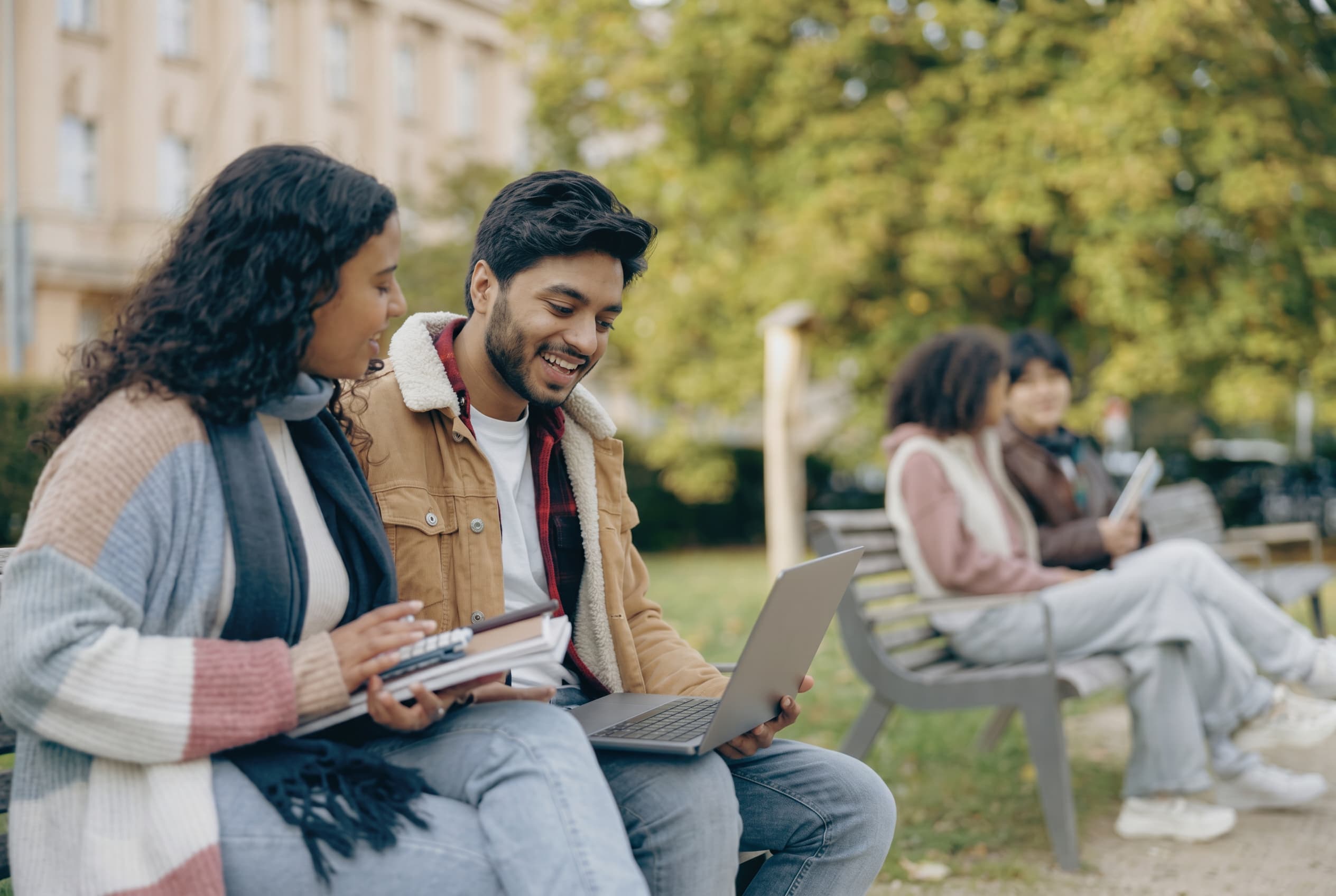 Two students planning next steps together on a bench with a laptop.