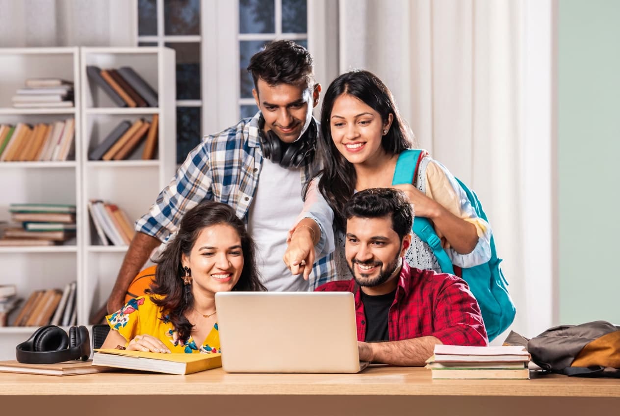 Four students from India gathered around a laptop, planning an application together.