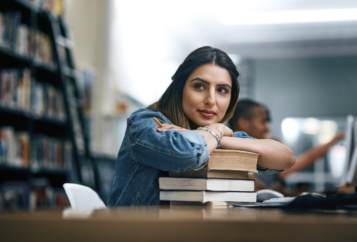 A student resting her chin on a stack of library books, thinking.